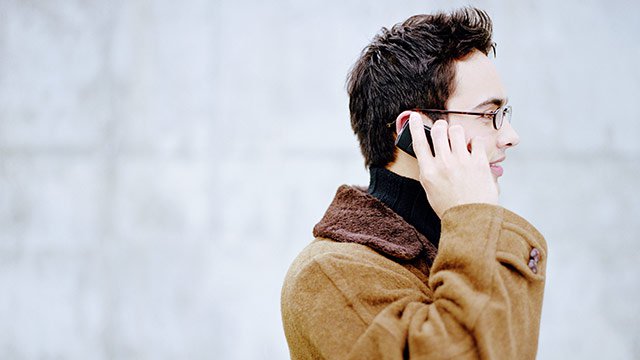 A man outside in a coat talking on his cellphone.