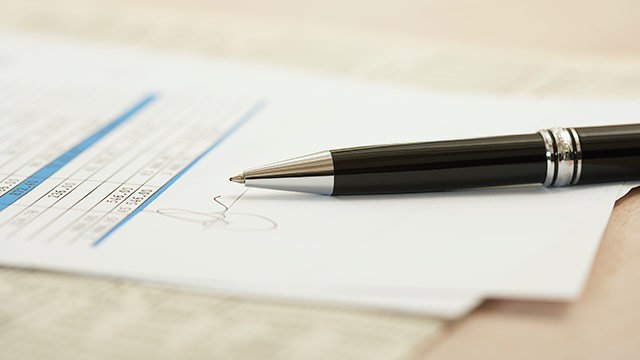 Closeup of a signed contract with a pen sitting on top.