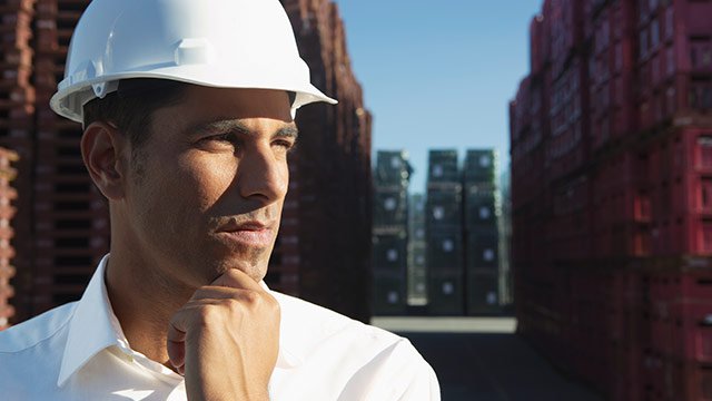A man in a shipping yard wearing a white construction hat.