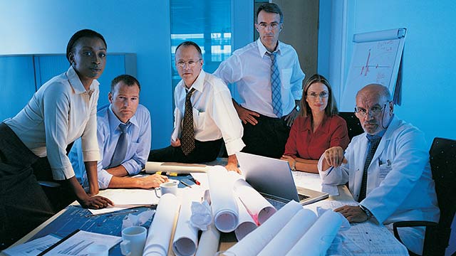 A group of employees looking at a table with a pile of rolled up blueprint papers.