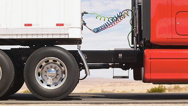 A semi-truck with a red cab and a white trailer.