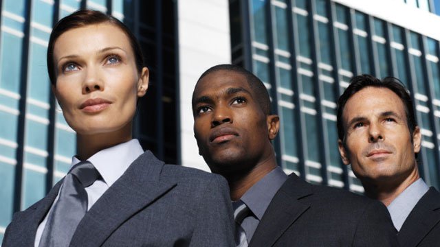 A group of three business professionals standing outside by a building.