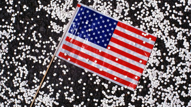 A small American flag sitting among small pieces of white confetti.
