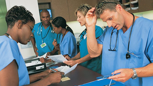 A group of medical professionals working together on paperwork wearing scrubs and stethoscopes.