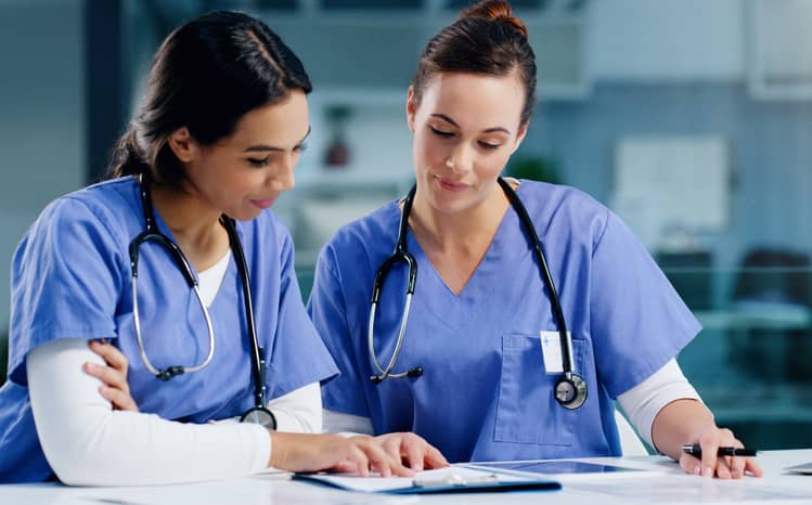 bpm in healthcare depicted by two nurses discussing business process management with a clipboard and tablet device in a healthcare facility
