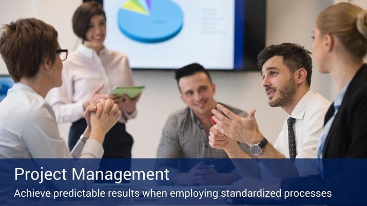 A group of business professionals speaking with each other and taking notes with a projection screen in the background with a pie chart on it.