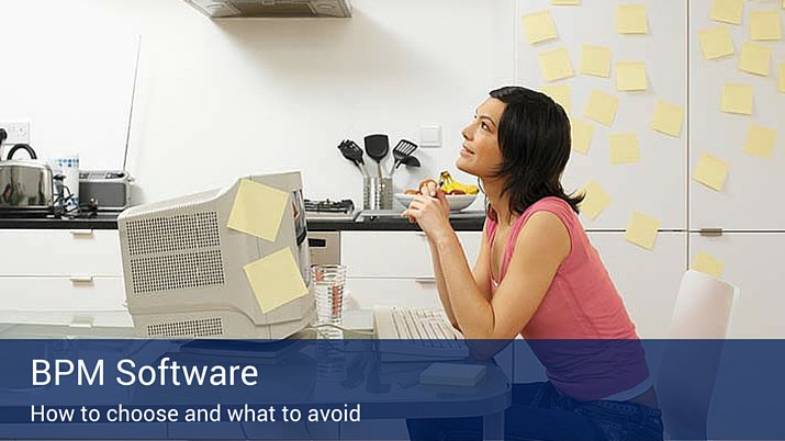 A woman looking up and thinking in her office with post-it notes all over her computer and the wall beside her.