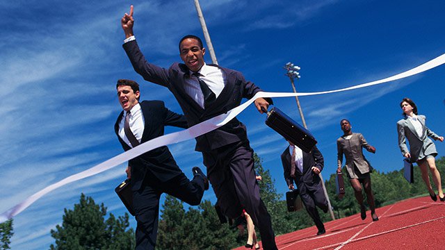 A group of business professionals, both men and women, running on a track and one of them is crossing the finish line while holding a briefcase and winning the race.