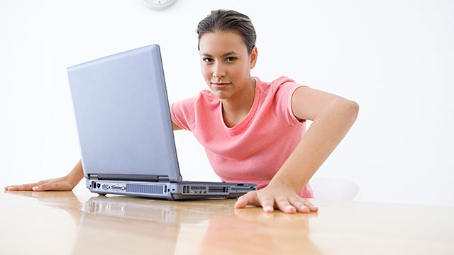 A woman sitting at her computer with her hands on the desk stretching.