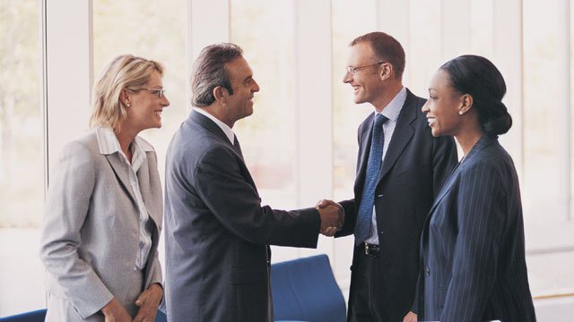 Four people coming together for a business meeting while two of them shake hands.