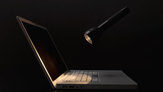 A flashlight shining on a laptop in a dark room.