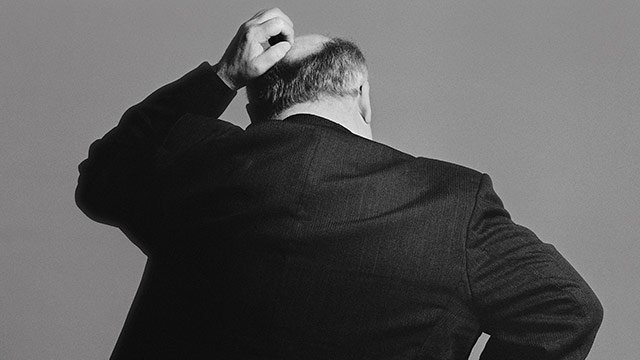View of the back of a businessman scratching his head.