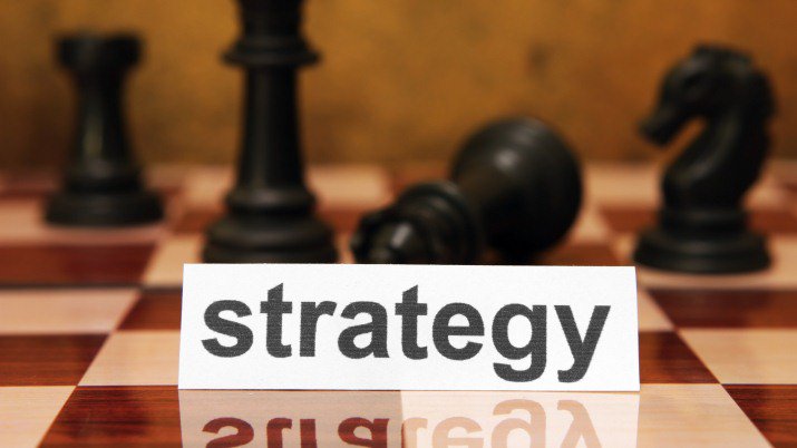 A chessboard with chess pieces scattered across the board and a white piece of paper on it that says strategy.