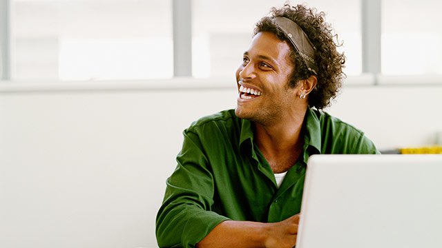A man looking up smiling and laughing while workingn on information security on his computer.