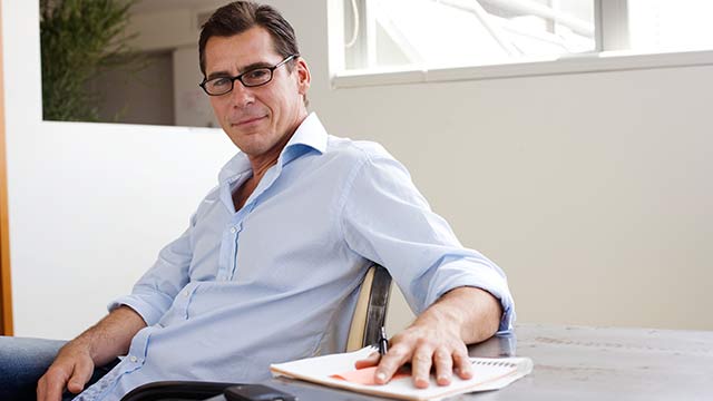 A man sitting in a chair at a table with his hand on a stack of papers.