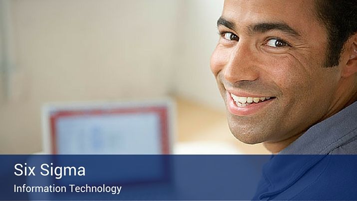 A man at a desk with his laptop looking back over his shoulder at the camera, with a blue banner on the botom of the image that reads "Six Sigma - information technology" in large white letters.