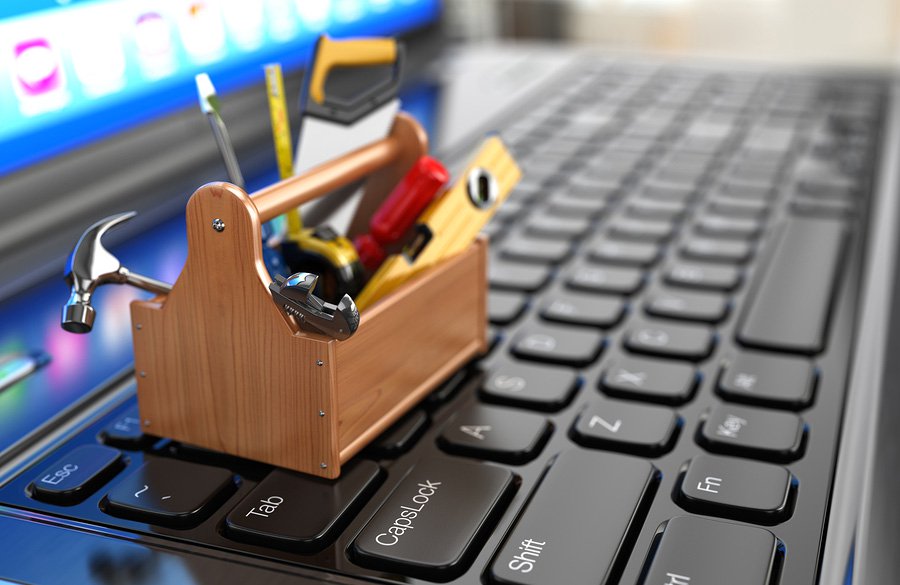 Close up of a very small toolbox on the the keyboard of a laptop filled with hammers, saws, levels, and other small tools.