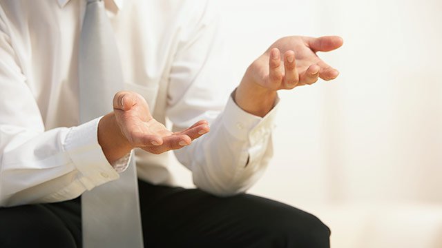 A partial shot of a businessman wearing a suit and gesturing with his hands while comparing six sigma and lean six sigma.