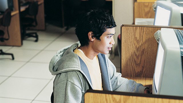 A student sitting at a computer in a computer lab with privacy desks.