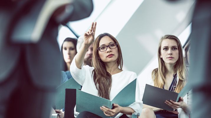 A small group of female HR students holding notebooks and listening to a lesson while one student is raising her hand.