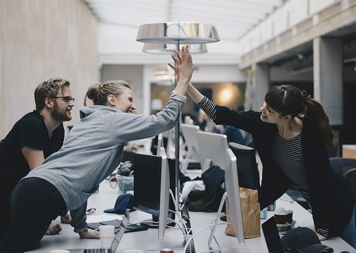 Project managers in an office space reaching across desks to congratulate each other with a high five.