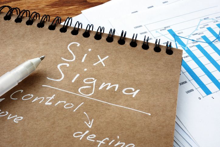 Six Sigma written on a notebook with process improvement charts in background