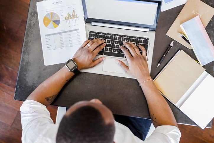 Man working on data reports using laptop at desk in home office